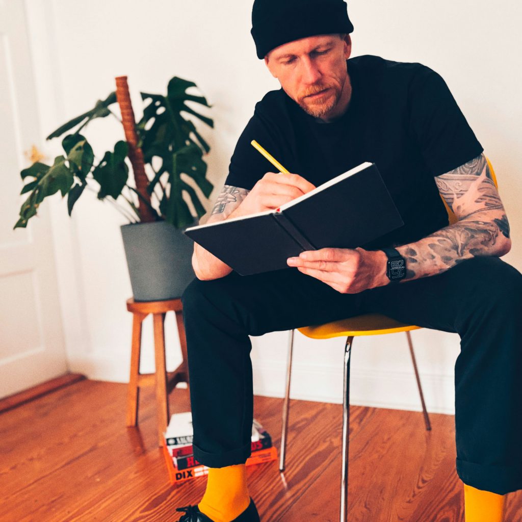 Thore Ketelsen, Künstler aus Lübeck, sitzt auf einem Stuhl und zeichnet in sein Skizzenbuch.
